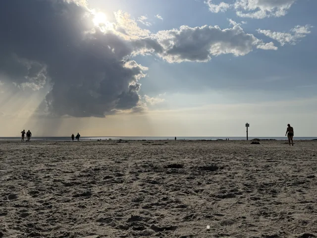 Weiter Nordseestrand mit Spaziergängern und Sonnenstrahlen zwischen den Wolken