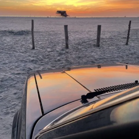 Blick über eine Motorhaube zum Sandstrand bei Sonnenuntergang